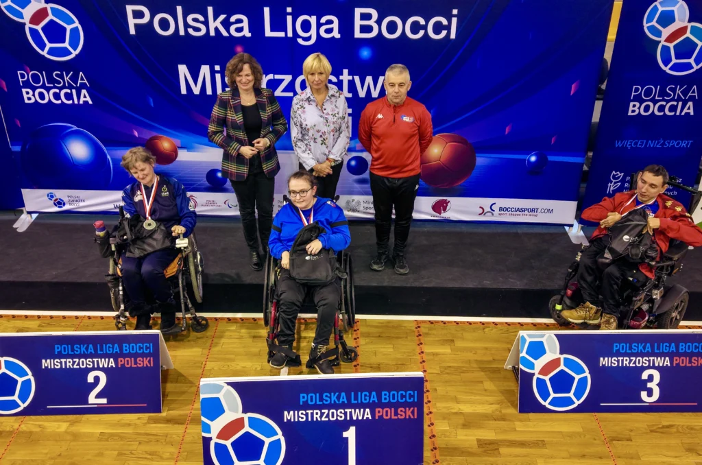 Ceremonia medalowa BC1 Mistrzostw Polski Boccia 2025: Wiktoria Herc z AKSON Zamość ze złotym medalem na najwyższym stopniu podium, srebrna Kinga Koza i brązowy medalista Robert Skwaryło z AKSON Zamość na tle ścianki Polskiej Ligi Bocci.