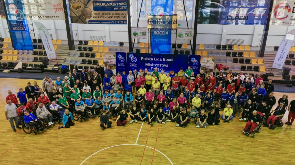 Zdjęcie grupowe uczestników Mistrzostw Polski Boccia 2025 wykonane z drona przez dronpolska.com, ukazujące wszystkie drużyny ustawione na parkiecie hali w Wągrowcu.