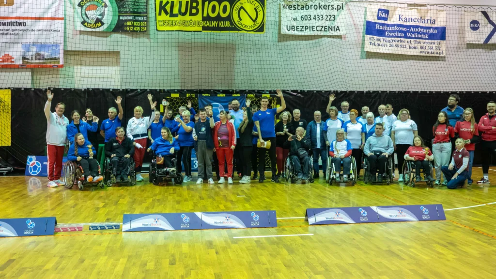 Duża grupa zawodników, trenerów i wolontariuszy pozuje razem na hali podczas Mistrzostw Polski Boccia 2025.